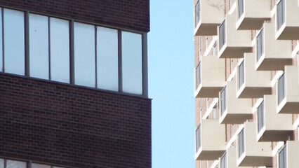 A close view of two contrasting buildings under a clear blue sky. On the left, a dark red brick building displays large, multi-paned windows.