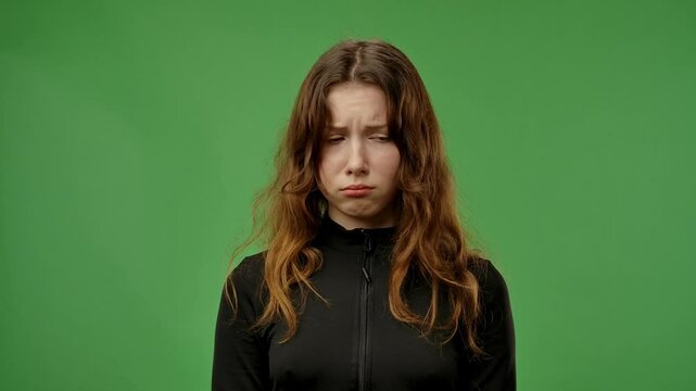 Teenage girl posing at camera with sad upset pouting face, teary expression, isolated on chroma key green screen studio background mockup. Slow motion