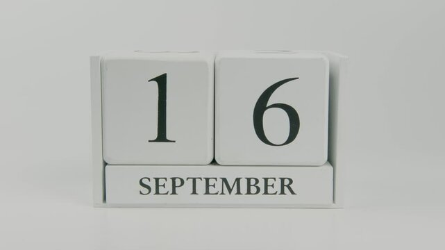 A hand flips a wooden calendar from September 16th to September 17th on a white background, marking the transition from one day to the next