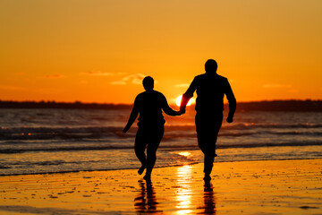 Silhouette of Playful Couple Running on Wet Beach Holding Hands at Golden Sunset with Sun Flare