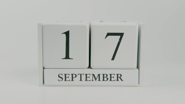 A hand flips a wooden calendar from September 17th to September 18th on a white background, showing the passage of time as the date changes
