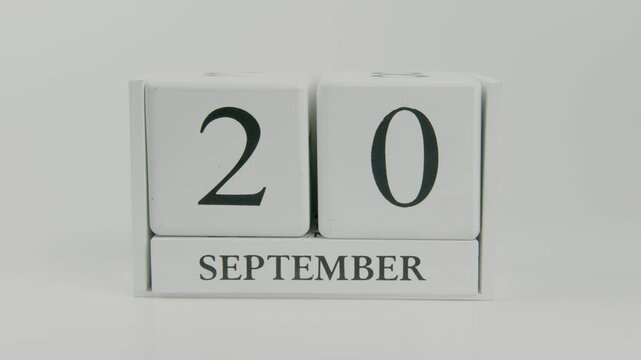 A hand flips a wooden calendar from September 20th to September 21st on a white background, marking the transition between days