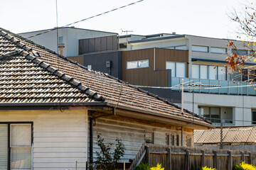 Contrasting newly built multi-story apartments against old weatherboard house with tiled roof in the foreground - themes of urban transformation, gentrification, and changing suburban character.
