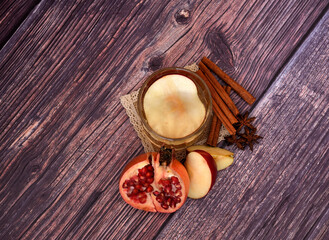 A glass of apple cider on a jute napkin with cinnamon and anise on a wooden table, next to pieces...