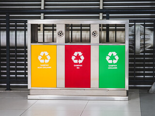 A set of colorful recycling bins labeled for non-organic, hazardous (B3), and organic waste in Indonesian. Stainless steel frame and modern urban background.