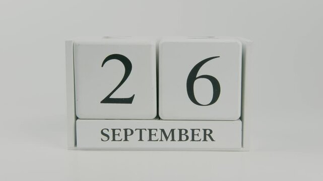 A hand flips a wooden calendar from September 26th to September 27th on a white background, representing the change of day