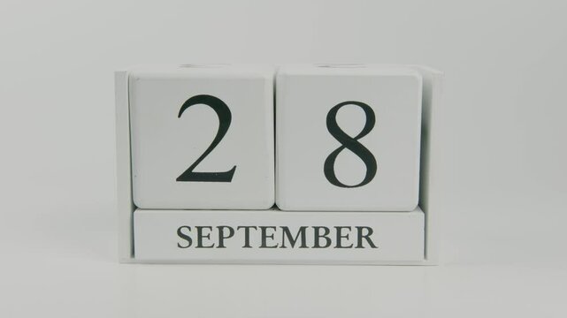A hand flips a wooden calendar from September 28th to September 29th on a white background, signaling the passage of time