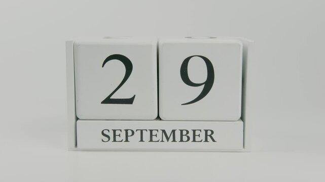 A hand flips a wooden calendar from September 29th to September 30th on a white background, marking the end of the month