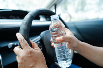 Asian woman driver hold cold water for drink in car, dangerous and risk an accident.