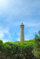 The Ke Ga Lighthouse in Vietnam stands tall above lush green foliage under a bright blue sky.