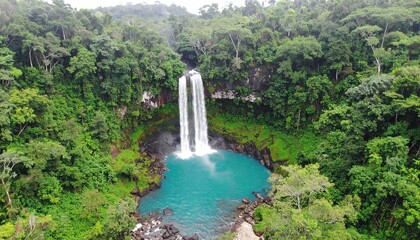 Lush waterfall cascades into a vivid turquoise pool surrounded by dense, green forest canopy