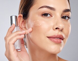 Woman applies cream on face, holding a sleek bottle against a neutral backdrop