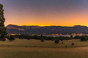 Obraz premium Serene twilight landscape with a mountain range and a calm lake, illuminated by the soft glow of sunset and stars