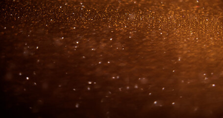 Bokeh light. Glowing trail. Defocused golden color sparkling glitter texture on shimmering dark abstract modern background.