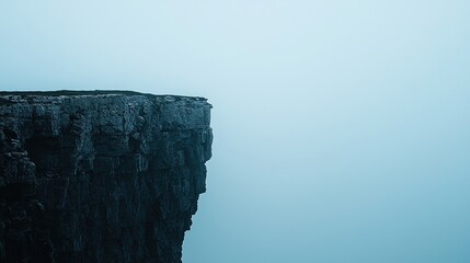 A steep rocky cliff edge stands against a misty, blue sky, evoking solitude and vastness.