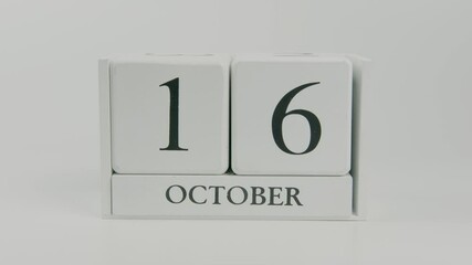 A hand flips the wooden calendar from October 16th to October 17th on a white background, showing the change to a new day