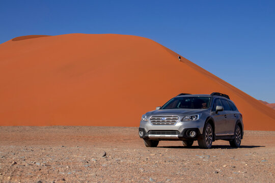 A grey Subaru Outback near a red sand dune on a hot sunny day