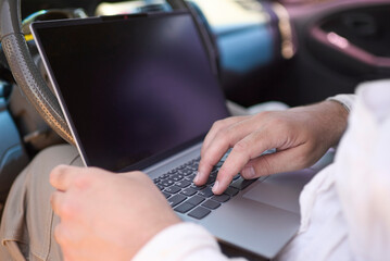 Close up of male hands using a laptop while sitting in his car, showcasing the concept of digital nomad, remote work and working while traveling, freedom lifestyle.