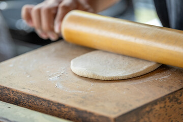 A person is rolling out dough on a wooden board
