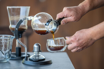 A person is pouring coffee into a cup from a glass container