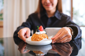 Closeup image of a woman serving a plate of strawberry choux cream in cafe