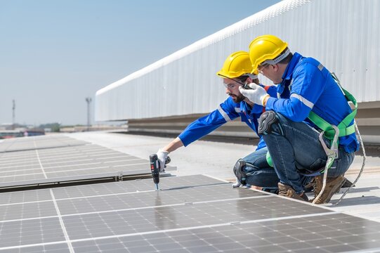 Two solar panel installation workers wearing safety gear are installing solar panels on a commercial building's roof.