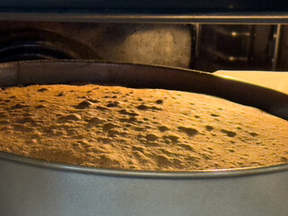 Cake batter baking in a round metal pan inside an electric oven, lined with parchment paper,...