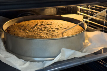 Sponge cake being tested for doneness with a skewer while baking in a round metal pan inside an oven, lined with parchment paper.