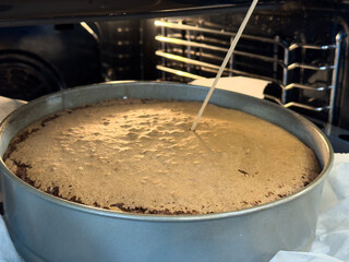 Sponge cake being tested for doneness with a skewer while baking in a round metal pan inside an oven, lined with parchment paper.