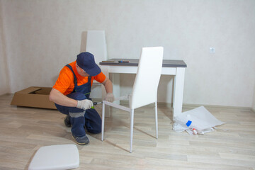 A middle-aged man in a special jumpsuit is assembling furniture out of a box
