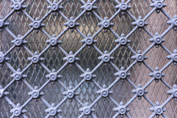 Fototapeta premium Decorative metal lattice with geometric and floral elements over diamond-patterned textured glass, creating a detailed and symmetrical architectural motif.