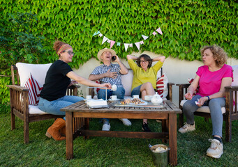 Middle-aged friends relaxing and laughing during backyard coffee time while enjoying tea and pastries together
