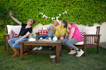 Middle-aged friends taking a selfie together while enjoying coffee and pastries in a cheerful backyard moment