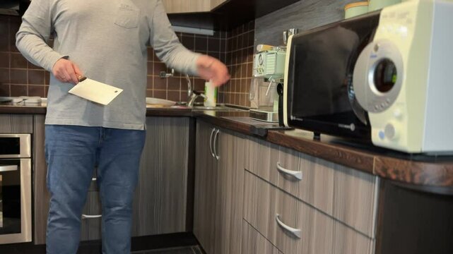 A man in the kitchen carefully wipes a clean meat cleaver with a cloth, preparing it for cooking.
