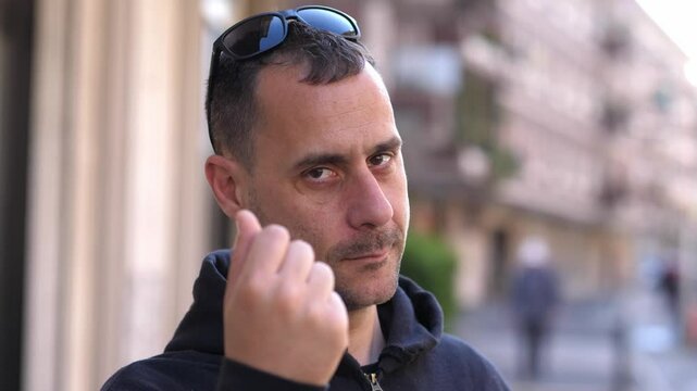 A man makes a classic money gesture, rubbing fingers together as if expecting to get paid for something
