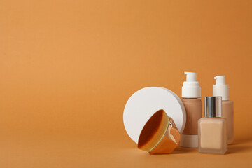 Bottles of foundation and cosmetic brush on orange background, space for text