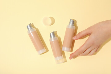 Bottles of foundation and female hand on beige background, top view