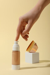 Bottle of foundation, cosmetic brush and female hand on beige background