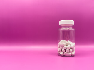 White pills in a transparent jar with a white lid for diseases on a bright pink background, stands...