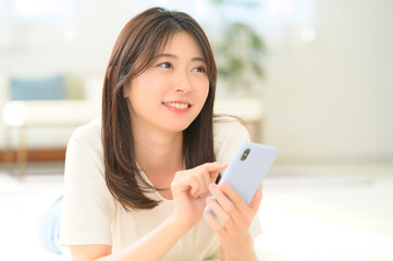 明るい部屋でスマートフォンを操作する女性が見せるくつろぎの笑顔