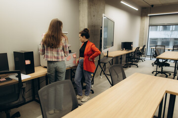 Two Women Collaborating in a Modern Office with Workstations and Technology