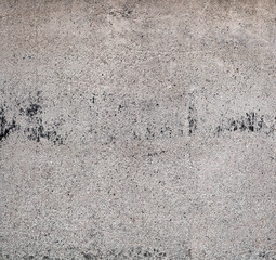 Exposed concrete surface with a clearly rough, irregular texture. The structure shows porous inclusions, fine cracks, shuttering board impressions and irregular shadows through the grainy surface.