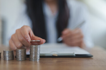 Businesswoman stacking coins while taking notes on financial growth