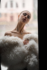Attractive young woman wrapped in fur coat,Portrait of sensual woman, near window