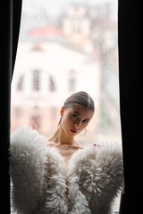 Attractive young woman wrapped in fur coat,Portrait of sensual woman, near window