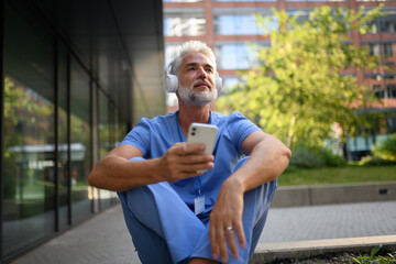 Healthcare worker relaxing with music outside hospital.