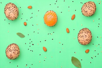 Colorful buns, almonds, and sesame seeds arranged on a mint-green background