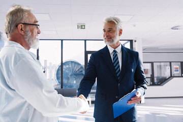 Doctor shaking hand with hospital manager, standing in hospital hallway.