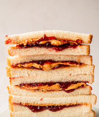 Close up of stack of peanut butter and jam sandwiches on white bread.