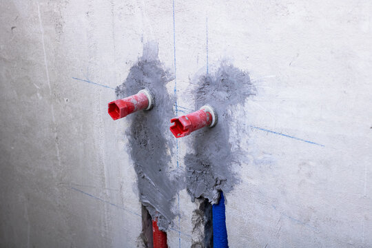 Two red pipes are currently connected to a sturdy concrete wall